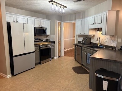 Kitchen featuring stainless steel appliances, dark countertops, backsplash, white cabinets, and a textured ceiling