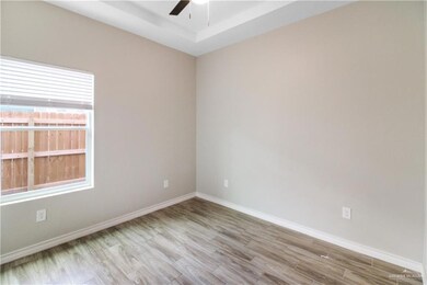 Empty room with ceiling fan, wood finished floors, baseboards, and a tray ceiling