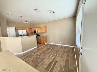 Kitchen featuring stainless steel appliances, dark wood-type flooring, brown cabinets, light countertops, and rail lighting