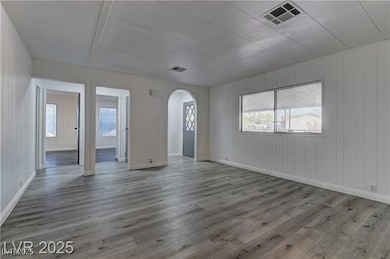 Unfurnished room with arched walkways, wood finished floors, and wood walls