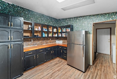 Kitchen with freestanding refrigerator, open shelves, wood counters, light wood finished floors, and wallpapered walls