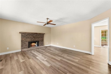 Unfurnished living room with ceiling fan, wood finished floors, a brick fireplace, and a textured ceiling