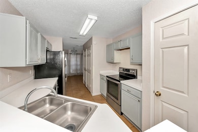 Kitchen with stainless steel appliances, light countertops, light tile patterned flooring, gray cabinetry, and a textured ceiling