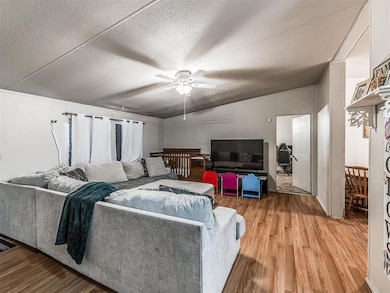 Living room with light wood-style floors, a ceiling fan, a textured ceiling, and lofted ceiling