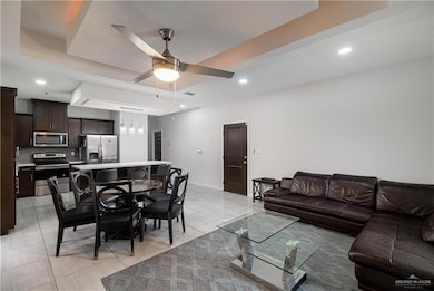 Living room with ceiling fan, a raised ceiling, light tile patterned floors, and recessed lighting