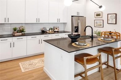 Kitchen featuring white cabinetry, decorative backsplash, light hardwood / wood-style flooring, a center island with sink, and stainless steel refrigerator with ice dispenser