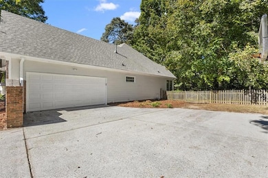 View of side of property featuring roof with shingles, driveway, brick siding, and a garage