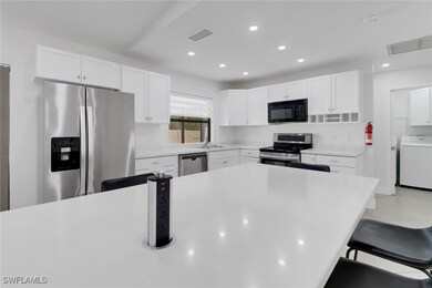 Kitchen featuring washer / clothes dryer, appliances with stainless steel finishes, white cabinets, and a kitchen breakfast bar