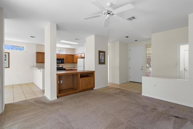 Unfurnished living room with light tile patterned flooring, light colored carpet, and a ceiling fan