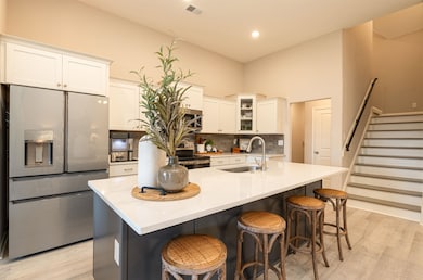 Kitchen featuring appliances with stainless steel finishes, light wood-style floors, backsplash, white cabinetry, and a kitchen bar
