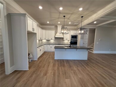 Kitchen with custom exhaust hood, double oven, quartz countertops, island with single bowl ss sink, pendant lighting over island, ornamental molding, recessed lighting, under cabinet lights, and stainless steel microwave