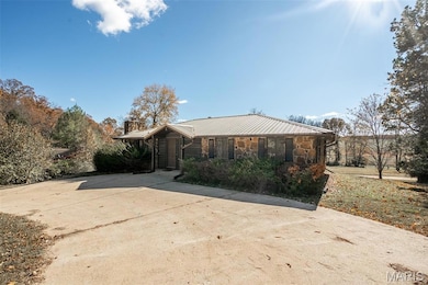 Ranch-style home featuring stone siding, a chimney, and a metal roof