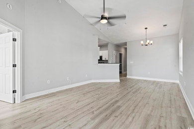 Unfurnished living room featuring light wood-style flooring, a ceiling fan, high vaulted ceiling, and a chandelier