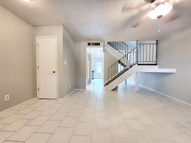 Unfurnished living room featuring a textured ceiling, stairway, ceiling fan, and light tile patterned floors