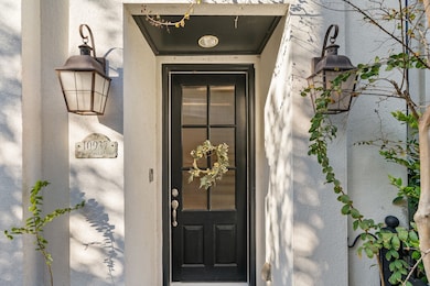 Walkway leads to a covered front door with lantern-style light fixture and a solid wood front door featuring privacy-frosted glass panels and a security camera doorbell.
