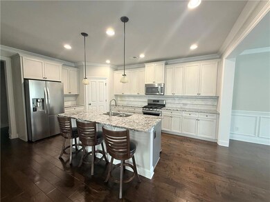 Kitchen with stainless steel appliances, crown molding, a kitchen island with sink, dark wood-style floors, and a kitchen bar