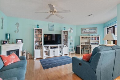 Living room with wood finished floors, ceiling fan, a glass covered fireplace, and a textured ceiling