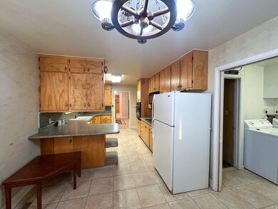 Kitchen with freestanding refrigerator, a peninsula, a breakfast bar, dark countertops, and brown cabinets