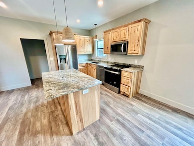 Kitchen with light brown cabinets, appliances with stainless steel finishes, a kitchen island, light stone counters, and recessed lighting