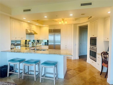 Kitchen with built in appliances, under cabinet range hood, a tray ceiling, a peninsula, and light stone countertops