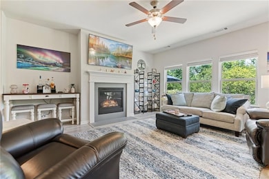 Living room with wood finished floors, ceiling fan, and a fireplace with flush hearth
