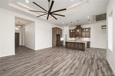 Kitchen with ceiling fan, a kitchen island with sink, hardwood / wood-style floors, pendant lighting, and a raised ceiling