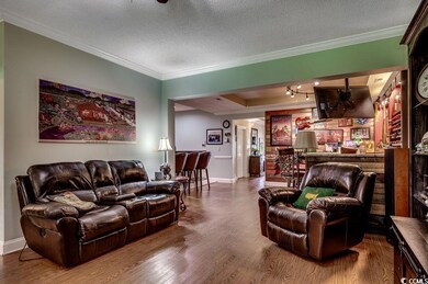 Living room featuring wood finished floors, crown molding, a textured ceiling, and a bar