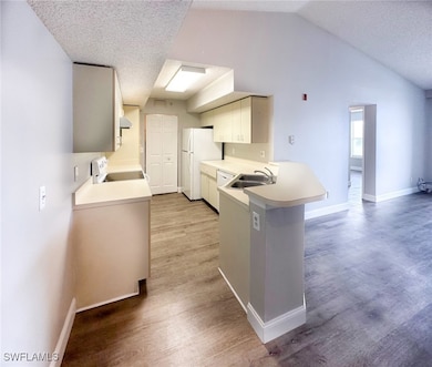 Kitchen featuring light countertops, a textured ceiling, a peninsula, light wood-style flooring, and white appliances