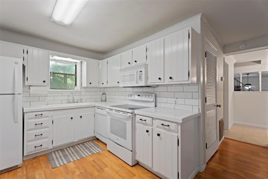 Kitchen featuring white appliances, light wood finished floors, decorative backsplash, white cabinets, and crown molding