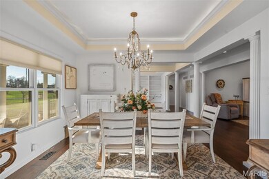 Dining area with wood flooring, a tray ceiling, crown molding, decorative columns, cove lighting and a chandelier