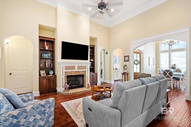 Living room featuring built in shelves, ceiling fan with notable chandelier, a brick fireplace, dark wood-type flooring, and ornamental molding