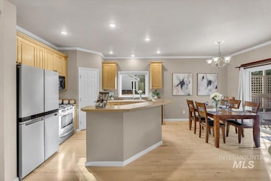 Kitchen featuring stainless steel appliances, a chandelier, light wood-style flooring, ornamental molding, and light brown cabinetry