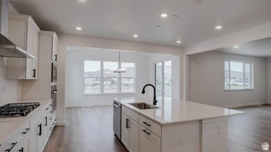 Kitchen featuring dark wood-type flooring, white cabinets, wall chimney exhaust hood, a chandelier, and an island with sink