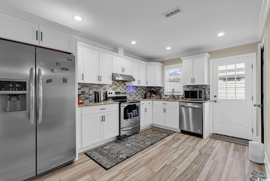 Kitchen featuring white cabinetry, ornamental molding, appliances with stainless steel finishes, and stone counters