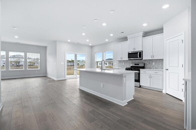 Kitchen featuring appliances with stainless steel finishes, dark wood finished floors, a center island with sink, light countertops, and tasteful backsplash