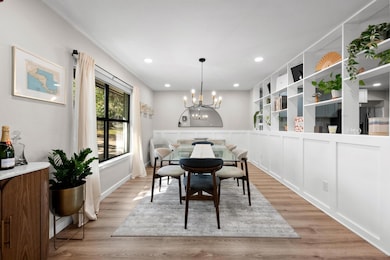 Dining area with light wood finished floors, a chandelier, recessed lighting, wainscoting, and a decorative wall