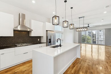 Kitchen with white cabinetry, wall chimney exhaust hood, decorative backsplash, appliances with stainless steel finishes, and hanging light fixtures