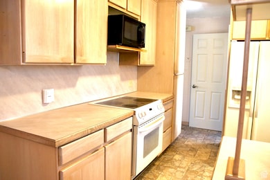 Kitchen with light brown cabinetry, white appliances, light countertops, and stone finish flooring
