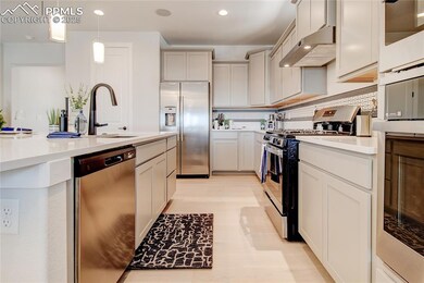 Kitchen with appliances with stainless steel finishes, exhaust hood, recessed lighting, pendant lighting, and light countertops