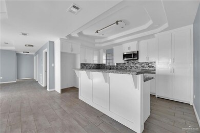 Main House Kitchen with a raised ceiling, white cabinets, a center island, a kitchen breakfast bar, and tasteful backsplash