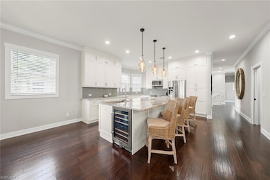 Kitchen featuring wine cooler, appliances with stainless steel finishes, a kitchen island with sink, backsplash, and white cabinets
