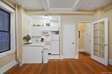 Kitchen with light wood-style floors, white cabinetry, white appliances, light countertops, and beamed ceiling
