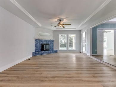 Unfurnished living room with a raised ceiling, a ceiling fan, light wood-type flooring, and a high end fireplace