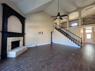 Unfurnished living room with high vaulted ceiling, wood tiled floors, a stone fireplace, stairway, and arched walkways
