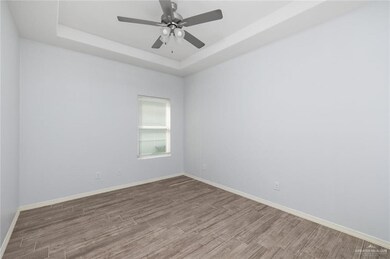 Unfurnished room featuring a tray ceiling, wood finished floors, and baseboards