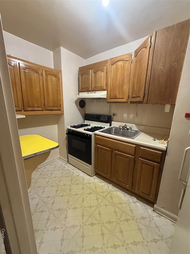 Kitchen featuring gas stove, light countertops, range hood, and brown cabinets