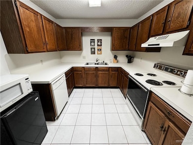Kitchen featuring under cabinet range hood, light countertops, light tile patterned flooring, white appliances, and a sink