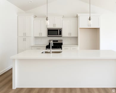 Kitchen featuring lofted ceiling, stainless steel microwave, an island with sink, stove, and white cabinets