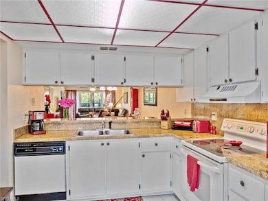 Kitchen featuring white appliances, white cabinetry, light countertops, and a drop ceiling