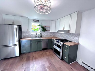 Kitchen featuring white cabinetry, appliances with stainless steel finishes, wooden counters, a baseboard radiator, and tasteful backsplash
